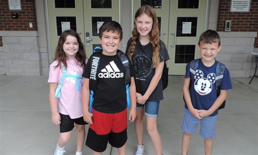 A group of elementary students stand in front of their school